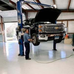 A man is taking the wheel off a large, black truck in the Milldale, CT workshop.