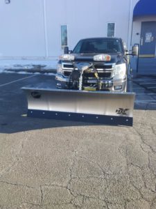 A straight plow by Fisher that has been attached to a large, black truck.