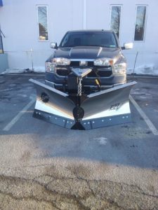 A Fisher v-plow that has been attached to a heavy-duty, black truck.