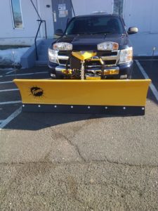 A yellow Fisher straight plow attached to a black truck.