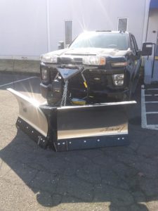 A large, black truck with a Fisher v-plow attached.
