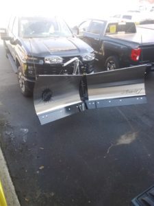 A Fisher v-plow attached to a large, black truck.