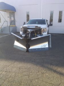 A white truck with a Fisher v-plow attached.