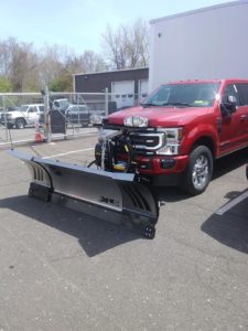 Heavy-duty truck with a straight plow attached to the front.