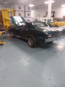 Black muscle car with the hood up in the shop.
